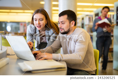 Man and woman spending time together in library, talking, work on laptop Man and woman spending time together in library, talking, work on laptop 143206525