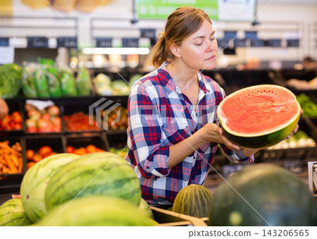 Positive woman customer choosing ripe watermelon in supermarket Positive woman customer choosing ripe watermelon in supermarket 143206565