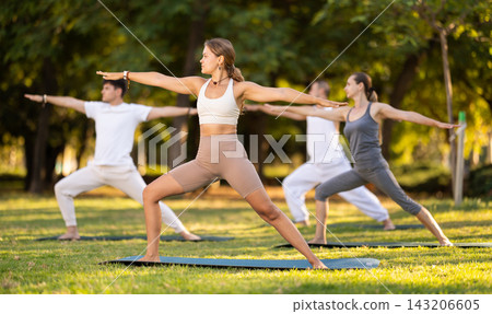 Yoga lesson visitors perform virabhadrasana in park Yoga lesson visitors perform virabhadrasana in park 143206605