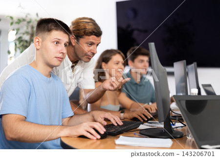 During computer lesson, male teacher helps guy student complete difficult task, During computer lesson, male teacher helps guy student complete difficult task, 143206701