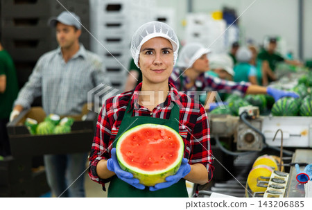 Cheerful woman fruit factory worker with half of ripe watermelon Cheerful woman fruit factory worker with half of ripe watermelon 143206885
