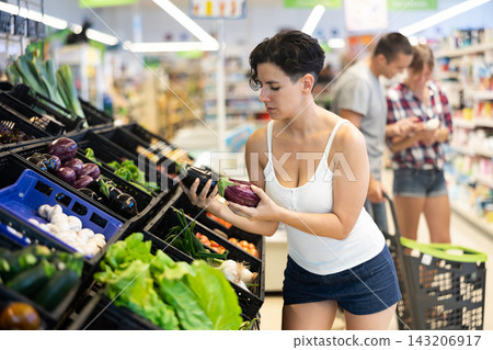 Woman choosing eggplants in supermarket Woman choosing eggplants in supermarket 143206917