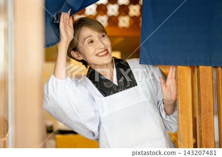 一位穿著和服的老婦人拉開暖簾,微笑著迎接顧客。 一位穿著和服的老婦人拉開暖簾,微笑著迎接顧客。 143207481