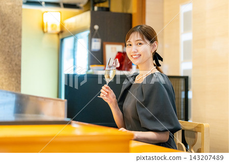 A young woman sits at the counter, holding a champagne glass. A young woman sits at the counter, holding a champagne glass. 143207489