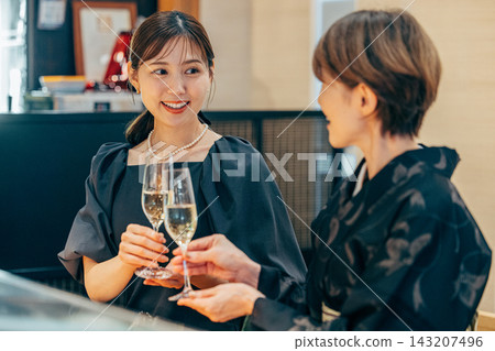 一對母女在壽司店舉杯慶祝：一位六十多歲的女士穿著和服，一位三十多歲的女士穿著連衣裙。 143207496