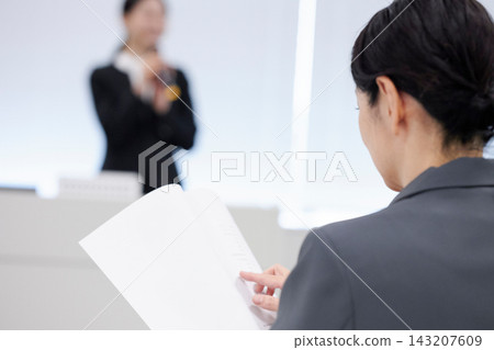 一位女士正在認真聽講,同時翻閱研討會資料。 一位女士正在認真聽講,同時翻閱研討會資料。 143207609