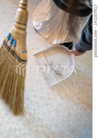 A woman sweeping the floor with a broom and dustpan. A woman sweeping the floor with a broom and dustpan. 143207617