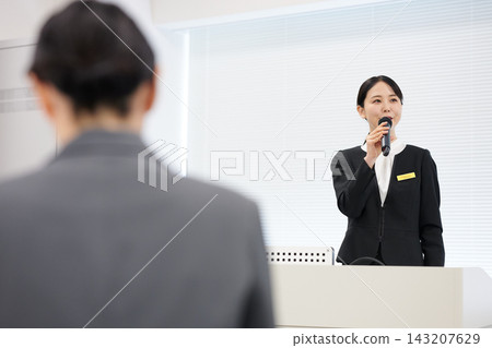 A businesswoman smiling and speaking at a podium with a microphone in hand, during a seminar. A businesswoman smiling and speaking at a podium with a microphone in hand, during a seminar. 143207629