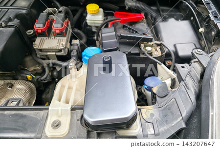Portable jump starter connected to car battery under open hood, no people. Concept of roadside assistance, emergency car repair, travel safety, road trip preparedness 143207647