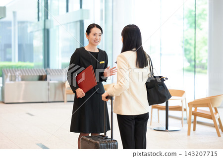 A staff member assists a woman with a suitcase in the hotel lobby. A staff member assists a woman with a suitcase in the hotel lobby. 143207715