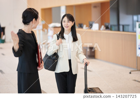 A female guest with a suitcase receives instructions from an attendant in the hotel lobby. A female guest with a suitcase receives instructions from an attendant in the hotel lobby. 143207725