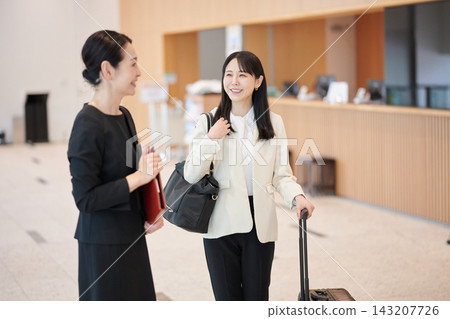 A woman with a suitcase is being guided by a staff member in the hotel lobby. A woman with a suitcase is being guided by a staff member in the hotel lobby. 143207726