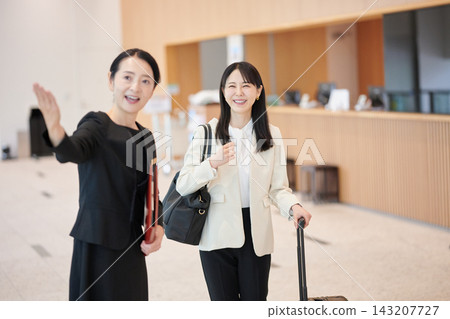 A front desk staff member smiles and guides a female guest in the hotel lobby. A front desk staff member smiles and guides a female guest in the hotel lobby. 143207727