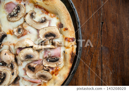 Cropped shot view of Italian mushrooms pizza serving on wooden table. Pizza, a staple of Italian cuisine, has become one of the most recognizable and popular dishes worldwide. Cropped shot view of Italian mushrooms pizza serving on wooden table. Pizza, a staple of Italian cuisine, has become one of the most recognizable and popular dishes worldwide. 143208020