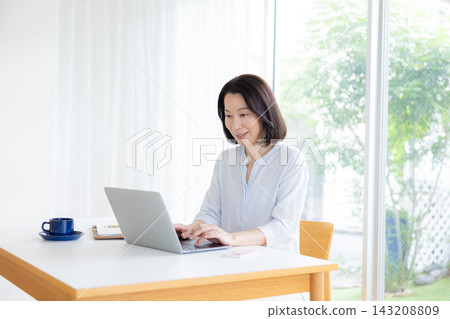 Middle-aged woman working remotely, looking at her computer screen. Middle-aged woman working remotely, looking at her computer screen. 143208809