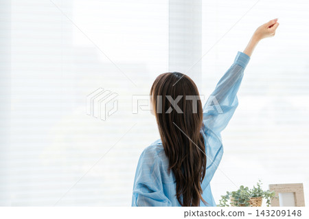 The back view of a young woman stretching comfortably by the window in the morning. The back view of a young woman stretching comfortably by the window in the morning. 143209148