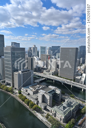 A landscape photograph capturing the cluster of skyscrapers and the urban landscape along the river in Yodoyabashi, Osaka, under a blue sky, in a vertical composition. [Osaka Landscape Photograph] 143209387