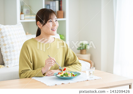 一位年輕女子在家吃沙拉 一位年輕女子在家吃沙拉 143209426