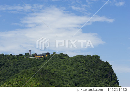 Buddhist temple and pagoda situated on a lush green forested mountain peak under a clear blue sky with white clouds Buddhist temple and pagoda situated on a lush green forested mountain peak under a clear blue sky with white clouds 143211480