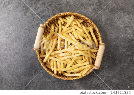 Top view of crispy golden french fries in a woven basket on a dark grey background 143211523
