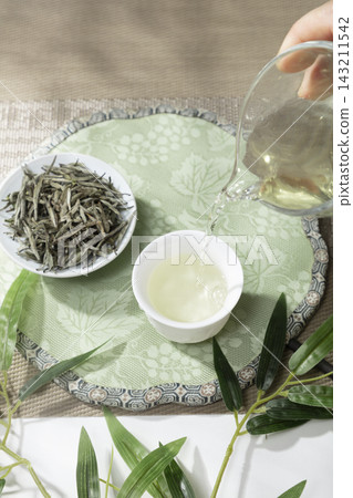 Pouring Chinese white tea from a glass pitcher into a white ceramic cup with dry silver needle tea leaves 143211542