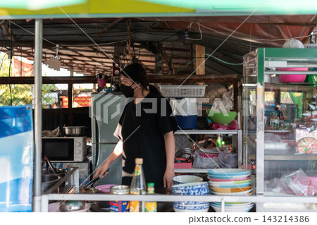 An LGBTQ woman wearing face mask prepares food at local noodle shop bowls utensils glass display case An LGBTQ woman wearing face mask prepares food at local noodle shop bowls utensils glass display case 143214386