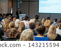 Audience facing a male speaker at a lectern 143215594