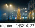 A brightly lit Christmas tree stands in a foggy, empty city square in Asti, Italy. 143216127