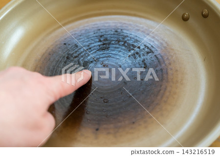 一隻手指著一個塗層破損、上面黏著燒焦食物的煎鍋。 一隻手指著一個塗層破損、上面黏著燒焦食物的煎鍋。 143216519