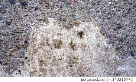Close up rough gray concrete wall texture with chipped plaster patch, embedded small stones, scattered debris, and worn weathered surface Close up rough gray concrete wall texture with chipped plaster patch, embedded small stones, scattered debris, and worn weathered surface 143216772