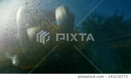 Moody night street scene with person silhouette behind foggy window glass and streetlight reflections on water droplets Moody night street scene with person silhouette behind foggy window glass and streetlight reflections on water droplets 143216773