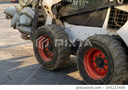 Skid Steer Loader Carrying Sandbags on Urban Pavement With Closeup Wheels and Tires 143221400