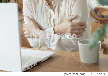 一位中年婦女在家工作時感到寒冷,抱緊雙臂。 一位中年婦女在家工作時感到寒冷,抱緊雙臂。 143222231