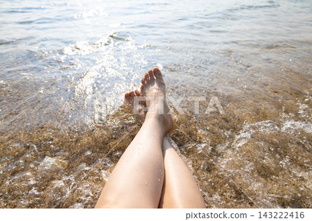 A woman's crossed legs are seen standing on a beach or at the water's edge in a tropical resort like Okinawa (Amami Oshima, Kagoshima Prefecture). A woman's crossed legs are seen standing on a beach or at the water's edge in a tropical resort like Okinawa (Amami Oshima, Kagoshima Prefecture). 143222416