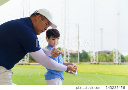 Golf instructor helping young Asian boy adjust swing posture at driving range Golf instructor helping young Asian boy adjust swing posture at driving range 143222456