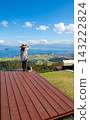 A woman stands with a stunning view of Lake Biwa in the background, holding her hat. 143222824