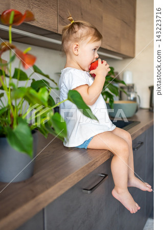 Baby girl blonde eating an apple in the kitchen, concept of healthy food for children 143223716