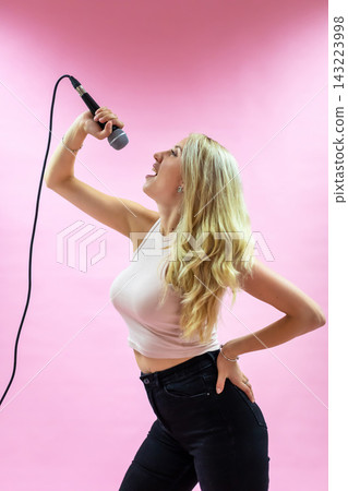 Beautiful young woman with microphone singing on pink background  143223998
