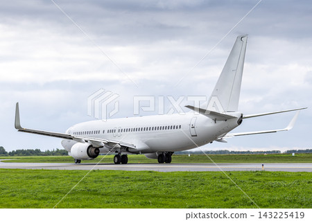White passenger airliner taxiing at the taxiway at the airport in cloudy weather White passenger airliner taxiing at the taxiway at the airport in cloudy weather 143225419