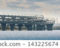 cars move along the expressway on poles in the water in clear sunny weather, lampposts above the road 143225674