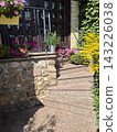 Beautiful granite steps featuring colorful potted petunias and lush foliage near the house doorstep. Picturesque residential front entrance with decorative garden flowers and stone wall. 143226038