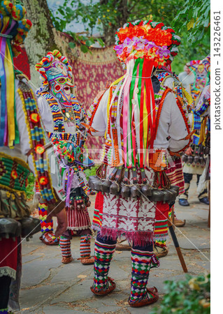 Kukeri Performer back view. Kukeri performers in colorful traditional Bulgarian folk costumes with ribbons, decorative mask, large cowbells. Balkan ritual clothing, cultural festival in Kotel Kukeri Performer back view. Kukeri performers in colorful traditional Bulgarian folk costumes with ribbons, decorative mask, large cowbells. Balkan ritual clothing, cultural festival in Kotel 143226461