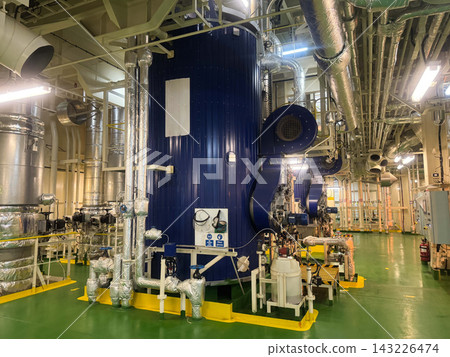 Industrial interior of vessel engine room displaying a large vertical marine auxiliary boiler with insulated steam pipelines. 143226474