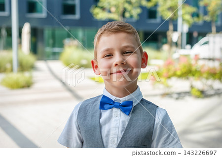 Child smiles while wearing a bow tie and vest in an outdoor setting with green plants around Child smiles while wearing a bow tie and vest in an outdoor setting with green plants around 143226697