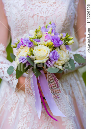 Bridal bouquet features white and purple flowers held by a woman in a lace dress Bridal bouquet features white and purple flowers held by a woman in a lace dress 143226706