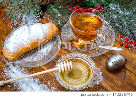 Christmas background, cup of tea with honey and croissant, branch of a Christmas tree in the snow Christmas background, cup of tea with honey and croissant, branch of a Christmas tree in the snow 143226746