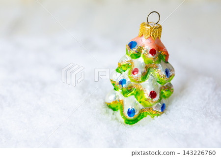Small glass Christmas tree ornament sits on white snow during winter season in a cozy home setting near holiday decorations and gifts Small glass Christmas tree ornament sits on white snow during winter season in a cozy home setting near holiday decorations and gifts 143226760