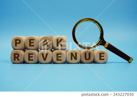 Peak Revenue alphabet letters wooden cube and magnifying glass on blue background Peak Revenue alphabet letters wooden cube and magnifying glass on blue background 143227030