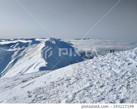 A climber gazing out from the summit of a snow-covered mountain, overlooking a sea of clouds and a chain of snow-covered peaks, and the magnificent snowscape. A climber gazing out from the summit of a snow-covered mountain, overlooking a sea of clouds and a chain of snow-covered peaks, and the magnificent snowscape. 143227199