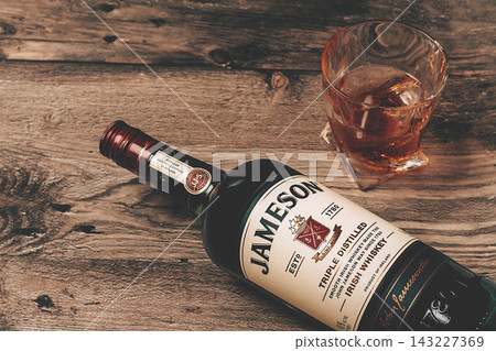 A bottle of whiskey is lying on a wooden table, next to it is a glass filled with temples and ice, there are no people A bottle of whiskey is lying on a wooden table, next to it is a glass filled with temples and ice, there are no people 143227369